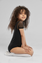 Girl in leotard sitting on studio floor.