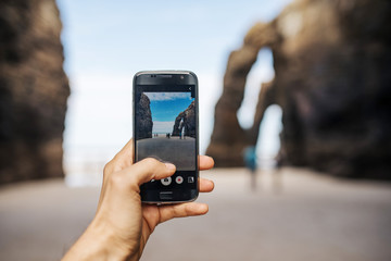 A young man takes a picture by phone. Playa de las Catedrales - Spain