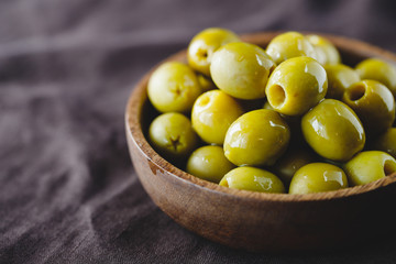 Green olives in a wooden bowl on a table, macro photography.