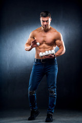 Handsome young sportsman is holding a packaging with eggs, healthy food protein. Gray background. Showing one egg to camera. Naked torso, healthy life concept.