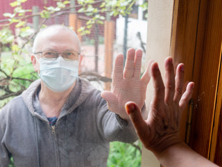 Elderly people in medical masks communicate through the window glass. New realities of communication in the world covered by the coronavirus pandemic.