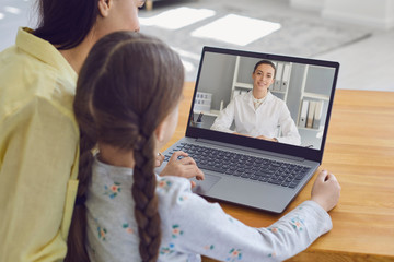 Family doctor online. Mother and girl kid talking consults a doctor using a laptop while sitting at home on the couch.