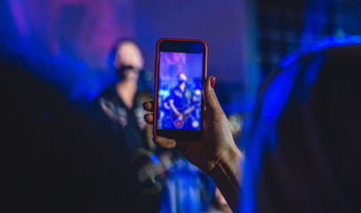 Woman at a concert in the club takes a photo on a smartphone