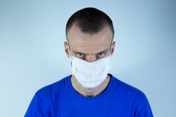 Young man in a protective mask on a blue background. Angry, stubborn, strict. Central location
