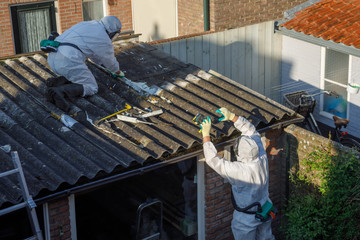 Professional asbestos removal. Man in protective suite removes asbestos roofing.