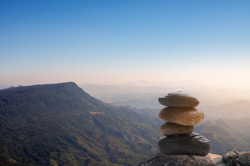 Stack of stones covered with moss on top of the mountain on a background of mountains covered with forests. Concept of balance and harmony. Stack of zen stones. Teamwork balance concept.