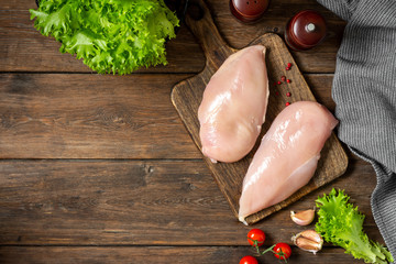 Chicken breast fillet on a wooden Board on a brown wooden table. Raw chicken breast. Top view with space for text - obrazy, fototapety, plakaty