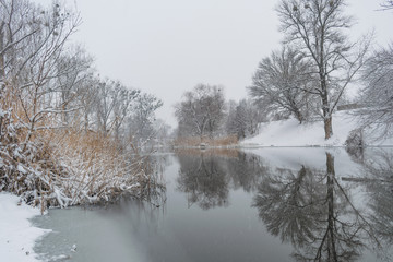 Winter landscape with snowfall on the river bank and a beautiful reflection in the river