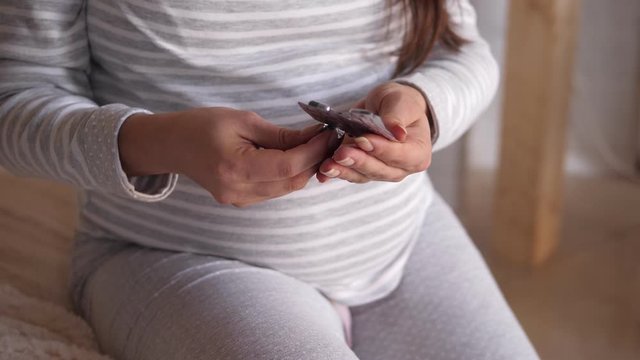 Pregnant woman holding medicine in the bedroom on the bed. Third trimester. Pregnant woman taking a medical pills. Close-up of pregnant woman with pills in her hand.
