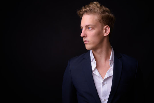 Face of young handsome blond businessman looking away against black background