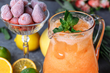 Summer fresh cold drink beverages. Ice Lemonade in the jug and lemons and orange with mint on the table outdoor. Orange lemonade in a jug