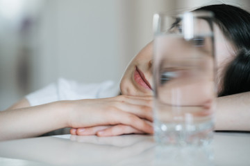 Portrait of a charming European girl of 8 years old. She is photographed through a glass of water. Trick shots with water. A photograph with a blurred background.