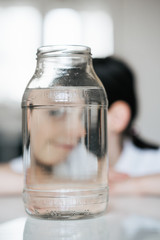 Portrait of a charming European girl of 8 years old. She is photographed through a glass of water. Trick shots with water. A photograph with a blurred background.