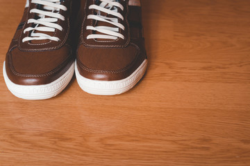 Man's shoes, casual, brown, with white laces, on wooden floor