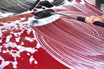 Red car washed in self serve carwash detail on brush moving over front hood, leaving strokes in...