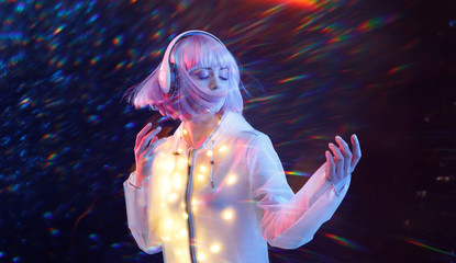 Beautiful woman with purple hair in futuristic costume over dark background. Neon light. Portrait of young girl in modern headphones listening music. Free space for text.