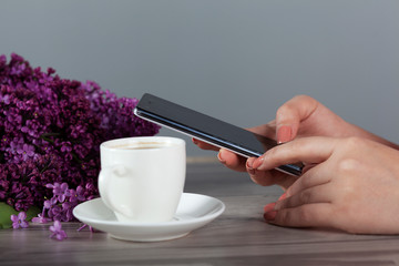 woman hand phone and coffee with lilac on table