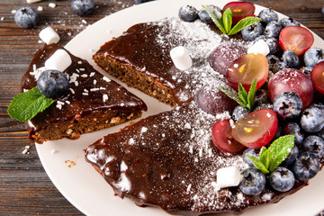 piece of cake, chocolate cake with fresh berries, blueberries, grapes, powdered sugar and mint on a white plate on a wooden ,   close up