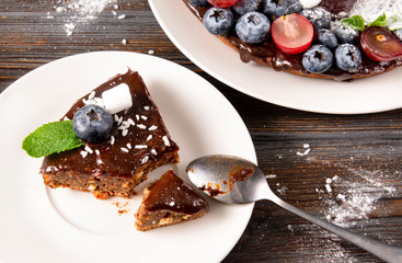 piece of chocolate cake with fresh berries, blueberries, grapes, powdered sugar and mint on a white plate on a wooden,  spoon