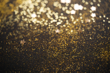 Beautiful Christmas light background. Abstract glitter bokeh and scattered sparkles in gold, on black