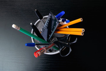 Metal stand with pencils, pens, scissors on wooden table