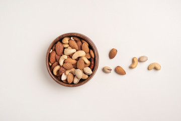 nuts almonds,  pistachio and cashews are placed in a wooden bowl on a light yellow background.