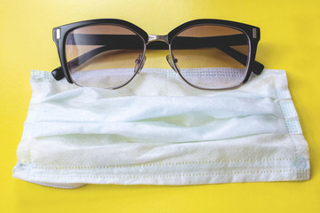 Black sunglasses and medical mask on yellow background