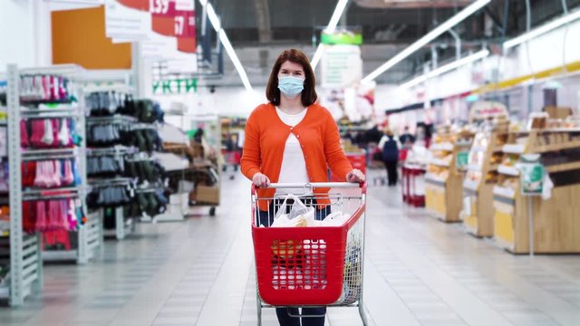Young woman in medical mask walking with shopping cart in supermarket