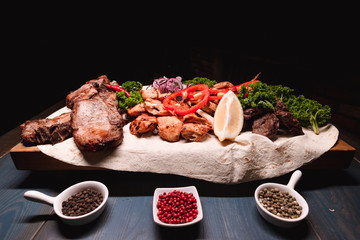 Appetizing fried meat lies on a wooden tray, among the seasonings. Studio photography of food in the cooking industry, dark background