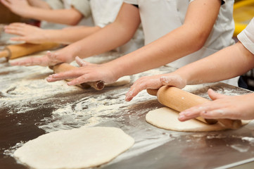 Little kids make dough products. Flour is scattered around. Hands close up.