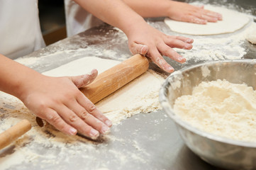 Little kids make dough products. Flour is scattered around. Hands close up.