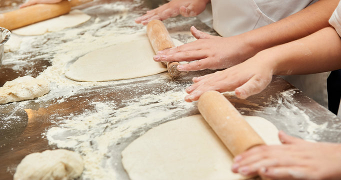 Little kids make dough products. Flour is scattered around. Hands close up.