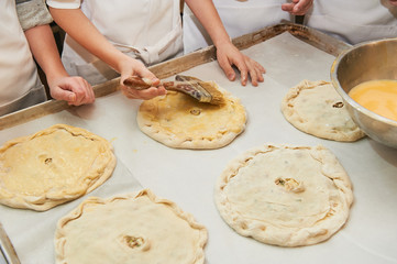 small children grease a dough product with an egg. Holding a brush