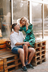 Fototapeta na wymiar Love story, a man and a blonde girl. Loving couple sitting hugging, looking at each other, smiling and laughing, on a European city street in summer. In casual wear. full-length portrait.