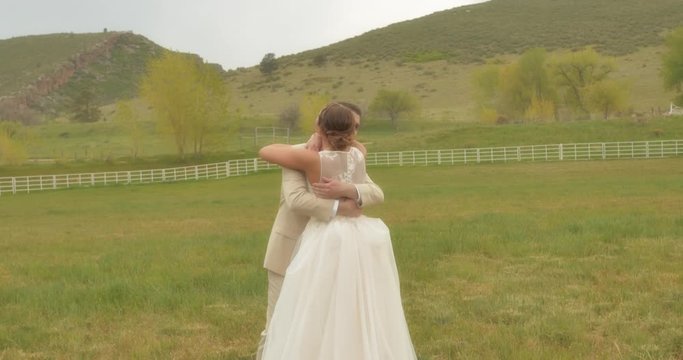 A bride taps her groom on the shoulder at their first look in a country Colorado field. He turns around and she bounces up and down giddily. They embrace,