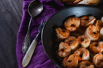Fried prawns in a pan on a table with bread, farm serving food, dark background. The concept of nutrition and beautiful serving of food
