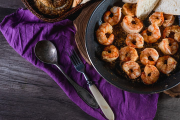 Fried prawns in a pan on a table with bread, farm serving food, dark background. The concept of nutrition and beautiful serving of food