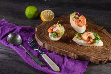 Sandwiches with shrimp, cheese and avocado on a wooden tray on the table, dark background. The concept of nutrition and beautiful serving of food