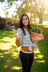 Beautiful dark haired smiling woman holding new orange pot with lavender and nice old garden hand trowel