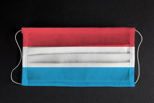 Coronavirus covid pandemic in Luxembourg. Flag of Luxembourg printed on medical mask on black background. National healthcare system concept. Covid-19 outbreak, quarantine in Luxembourg, Europe.