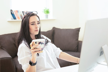 Portrait of attractive dark haired woman drinking coffee while working from home, reading emails on laptop ,  freelance  beautiful businesswoman making money from home