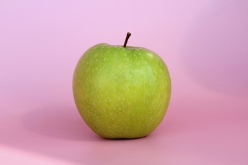 Green yellow apple on a pink background. Juicy ripe beautiful fruit.