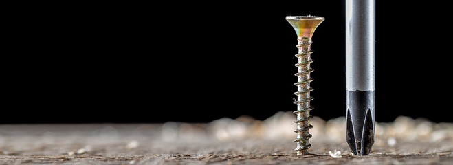 The screw and screwdriver close up on black background. Joinery and construction work. Panoramic banner.