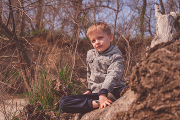 Solo traveller - young boy hiker in spring forest, sitting by an old decaying tree and looking into the distance