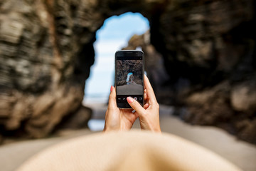 Young woman taking a picture by phone. Playa de las Catedrales - Spain