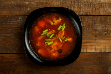 Black dish of italian tomato soup with potato and mushrooms on a wooden table.