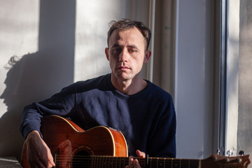 Obraz premium Guy with a guitar near the window.