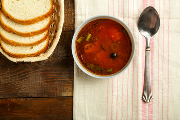 A light cup of Italian tomato soup with potatoes and mushrooms on a wooden table on a napkin and a spoon and bread.