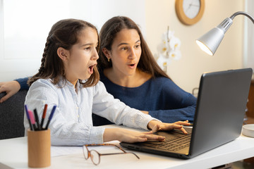 Two excited sisters checking contents of laptop at home