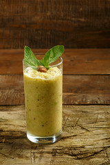 A glass of green smoothie on a wooden table on a napkin near fruits and nuts.